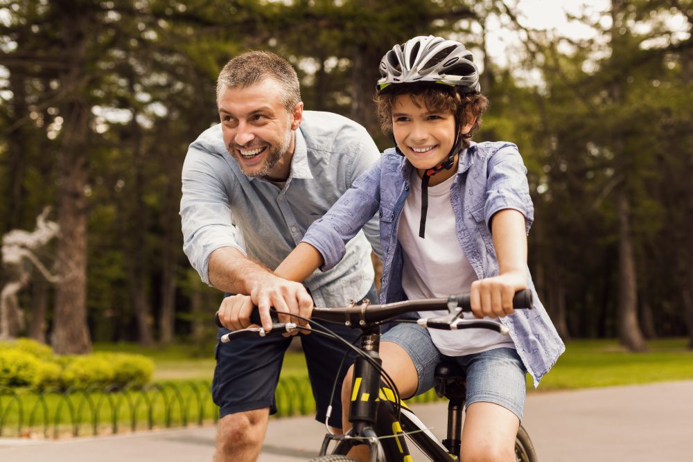 Dad teaching old child how to ride a bike AdobeStock 377660932